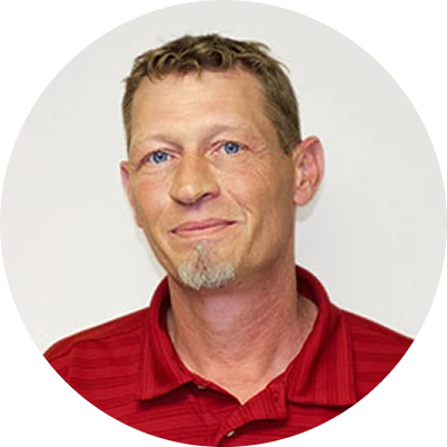 Man with short light brown hair, light facial hair, and blue eyes wearing a red collared shirt, posed against a plain white background.