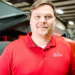 A man in a red collared shirt with an SCI logo stands indoors, with industrial equipment in the background.