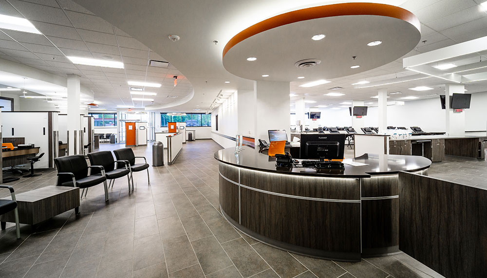 Modern office lobby of the Biotest Plasma Center with a circular reception desk, black chairs in a waiting area, and open workstations in the background, all brightly lit for a welcoming plasma donation experience.