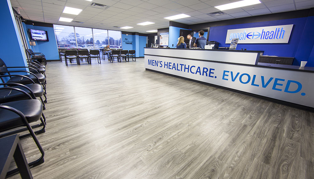Spacious Epoch Health Center men's healthcare clinic waiting area with rows of black chairs, a reception desk, and people standing near the counter.