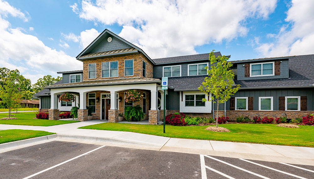 Two-story building with brick and siding exterior, covered entrance, landscaped lawn, and empty parking spaces in front under a partly cloudy sky.