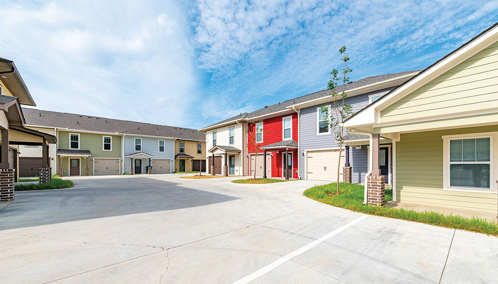 A row of modern townhouses with driveways and garages, featuring various exterior colors under a partly cloudy sky, brings a fresh look to the charm of Old Conway Village.